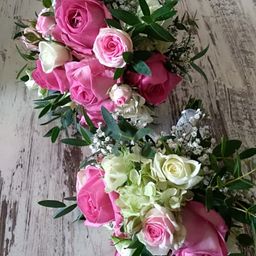 Eine Sammlung von rosa und weißen Rosen mit Babys Atem und grünen Blättern auf einer rustikalen Holzoberfläche arrangiert.
