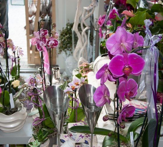 Eine Ausstellung von lila Orchideen mit rosa Bändern und silbernen Vasen. Eine Person steht im Hintergrund.