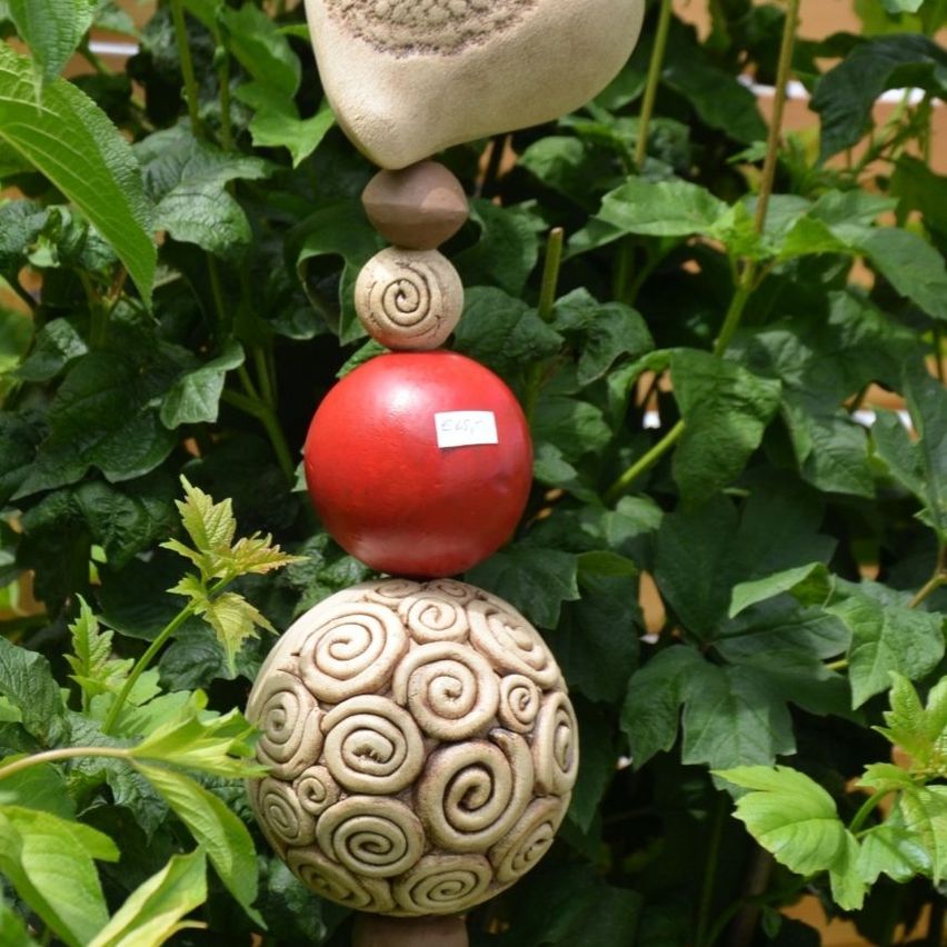 Ein Stapel von Tonfiguren mit einer roten Kugel in der Mitte, umgeben von spiralförmigen Kugeln, auf einem grünen Pflanzenhintergrund platziert.