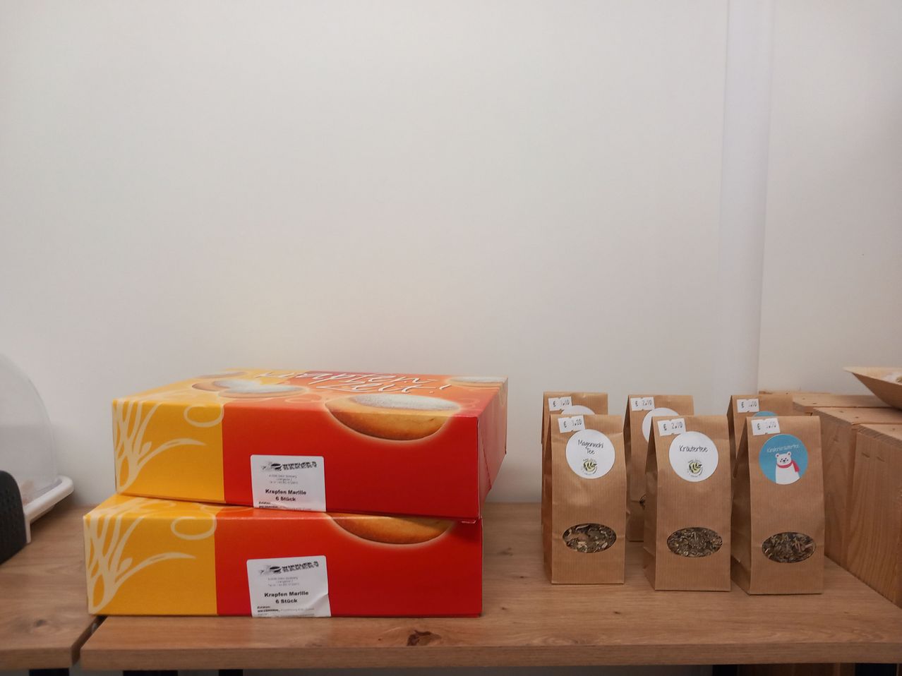 Two stacked orange and yellow boxes with white labels sit next to several brown paper bags with price tags on a wooden table against a white wall.