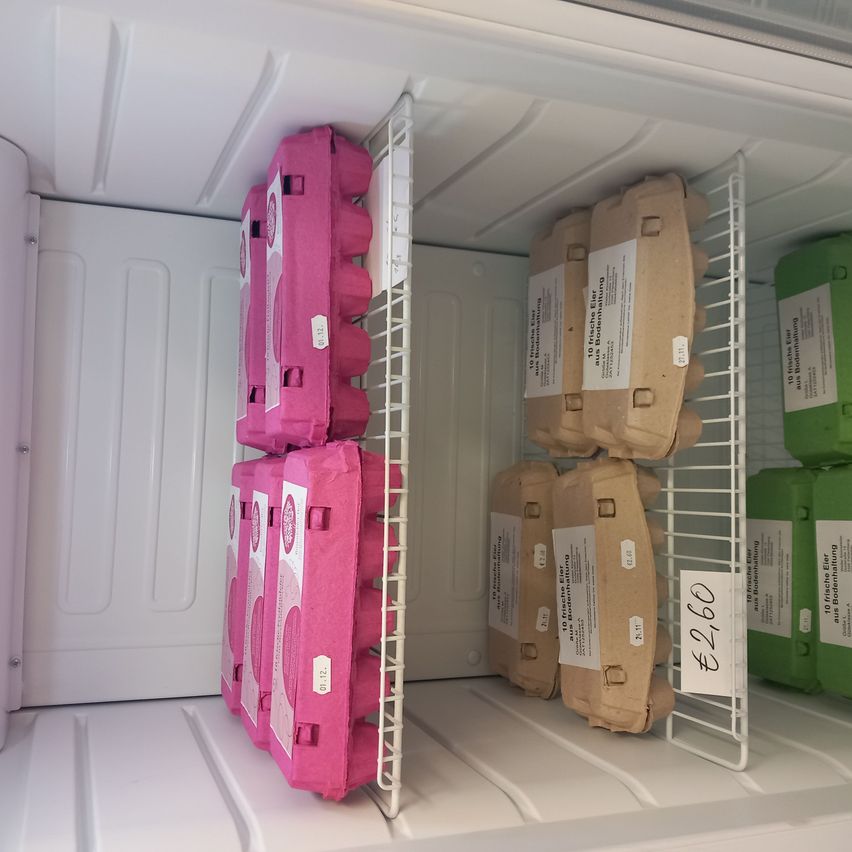 The inside of a refrigerator with egg cartons in pink, brown, and green colors. The pink cartons are stacked on the left, while the brown and green cartons are on the right.