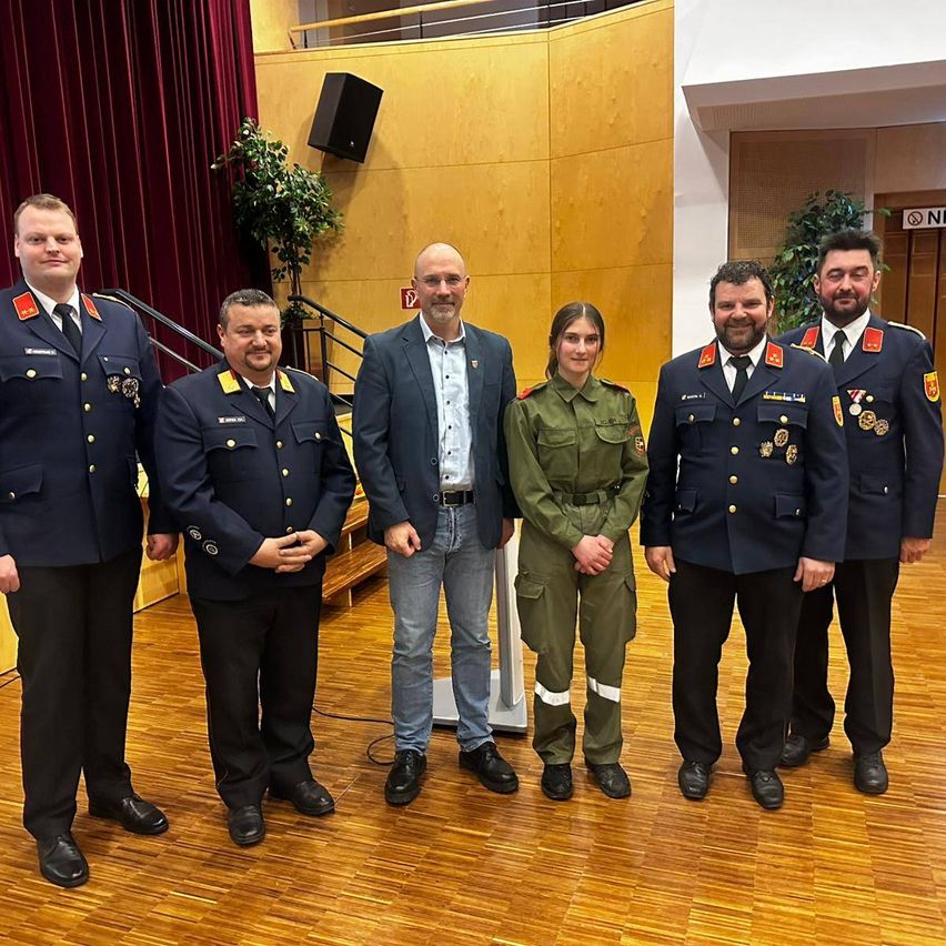 Five men and a woman in uniform stand together in a room. The woman is in the middle, and they all appear to be posing for a photo.