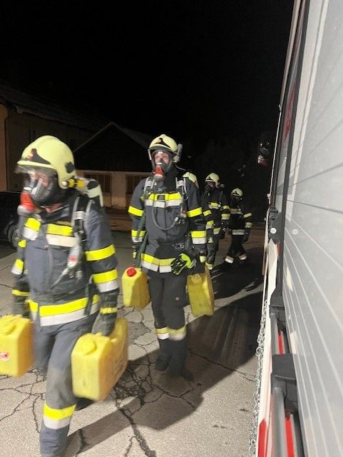 Feuerwehrleute in Schutzkleidung gehen mit gelben Containern auf der Straße.