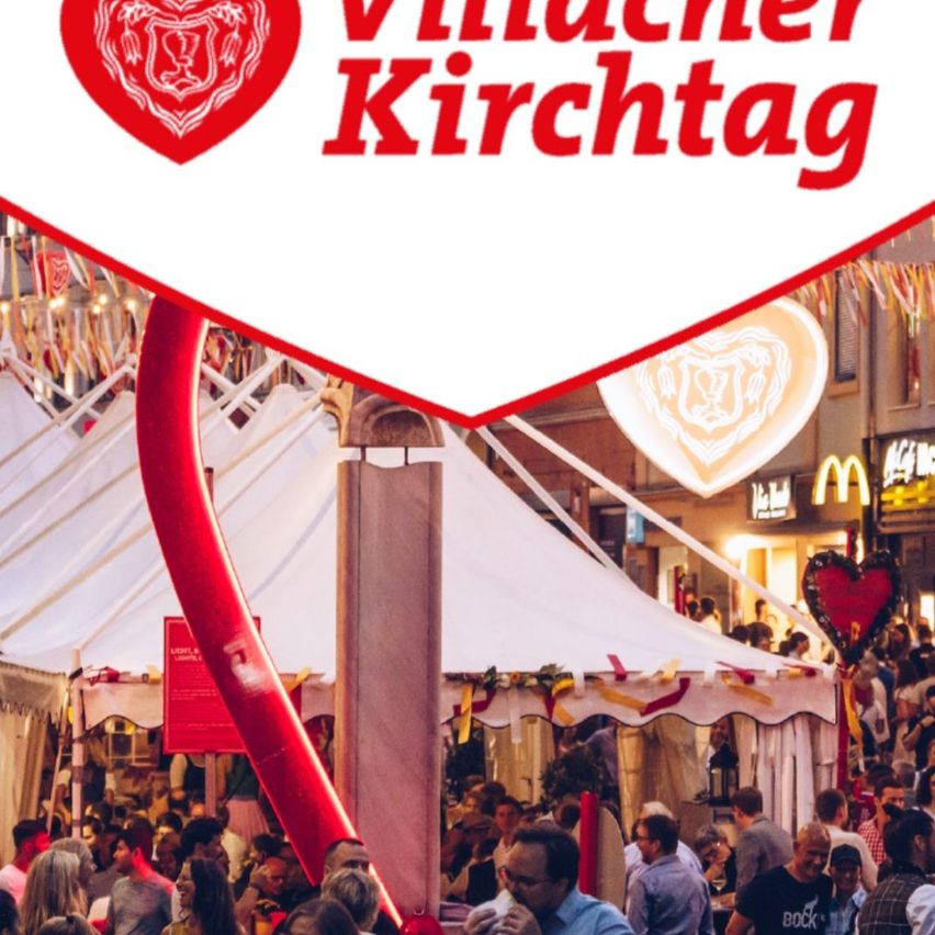 Eine Menschenmenge versammelt sich bei einer Freiluftveranstaltung unter einem großen weißen Zelt. Das Schild sagt Vinacher Kirchtag. Ein McDonald's-Schild ist im Hintergrund zu sehen.