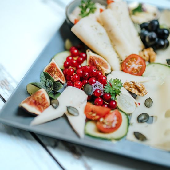 Ein Teller zeigt eine Auswahl an Lebensmitteln, darunter Käse, Feigen, Beeren, Tomaten, Gurken und Nüsse.