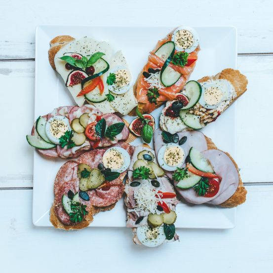 Ein weißer Teller mit einer Auswahl an Sandwiches. Jedes Sandwich enthält verschiedene Zutaten wie Eier, Käse, Gurken, Tomaten und Fleisch.