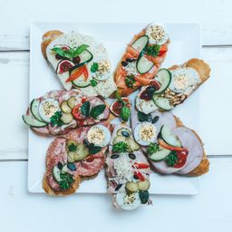 Ein weißer Teller mit einer Auswahl an Sandwiches. Jedes Sandwich enthält verschiedene Zutaten wie Eier, Käse, Gurken, Tomaten und Fleisch.