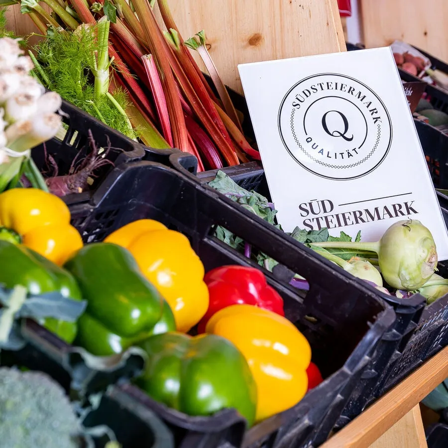Verschiedene Gemüsesorten wie Paprika, Brokkoli und Rüben sind in schwarzen Kisten ausgestellt, auf denen ein Schild mit der Aufschrift 'Südsteiermark' steht.