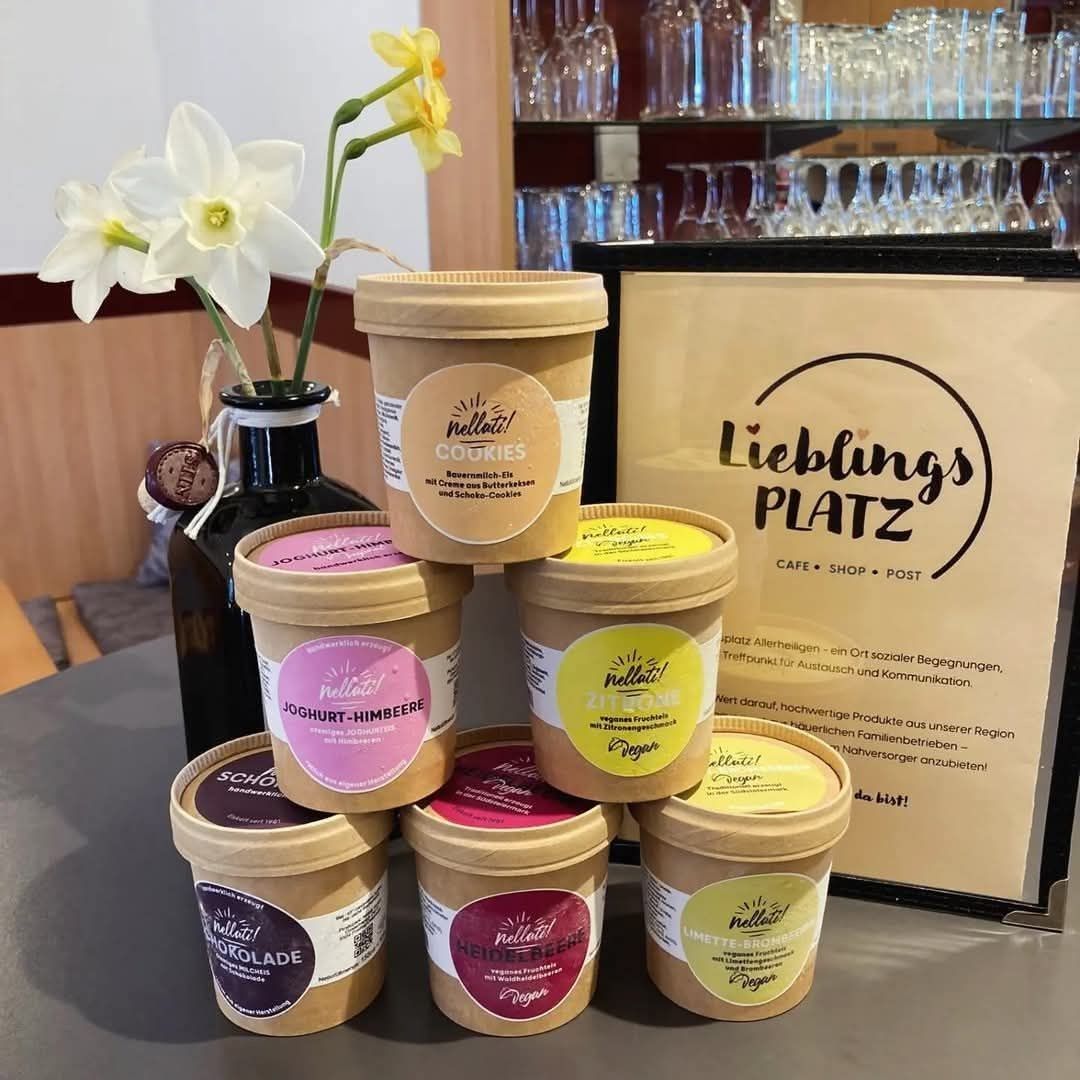 Ein Tisch mit mehreren Behältern von Nellal-Joghurt mit verschiedenen Geschmacksrichtungen, einer Vase mit Narzissen und einem Schild, das Lieblings Platz Café Shop Post sagt.