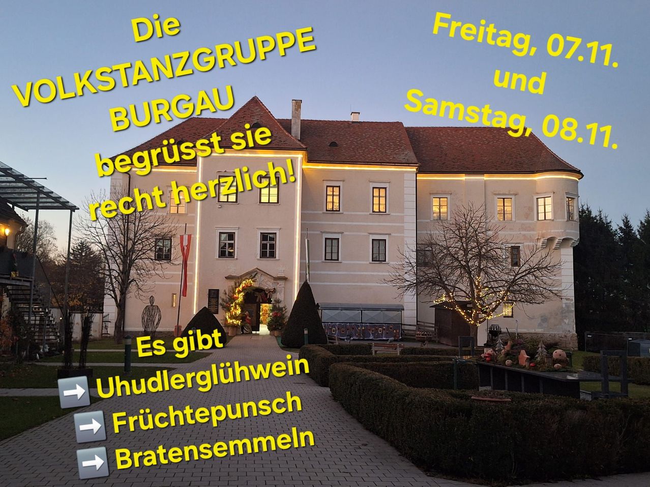 Ein großes weißes Gebäude mit einem braunen Dach, nachts beleuchtet. Es hat viele Fenster und ist von Hecken umgeben. Der Text lautet, 'Die Burgau heißt Sie herzlich willkommen'.