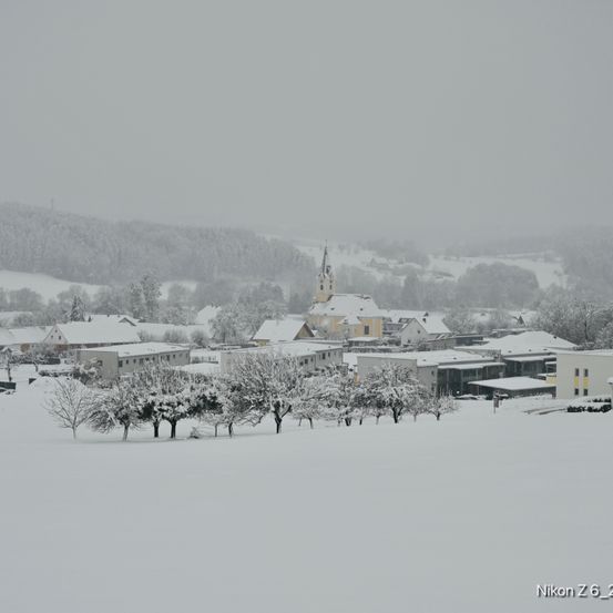 Schnee bedeckt eine kleine Stadt mit einer Kirche, umgeben von Hügeln und Bäumen, aufgenommen mit einer Nikon Z6-Kamera.