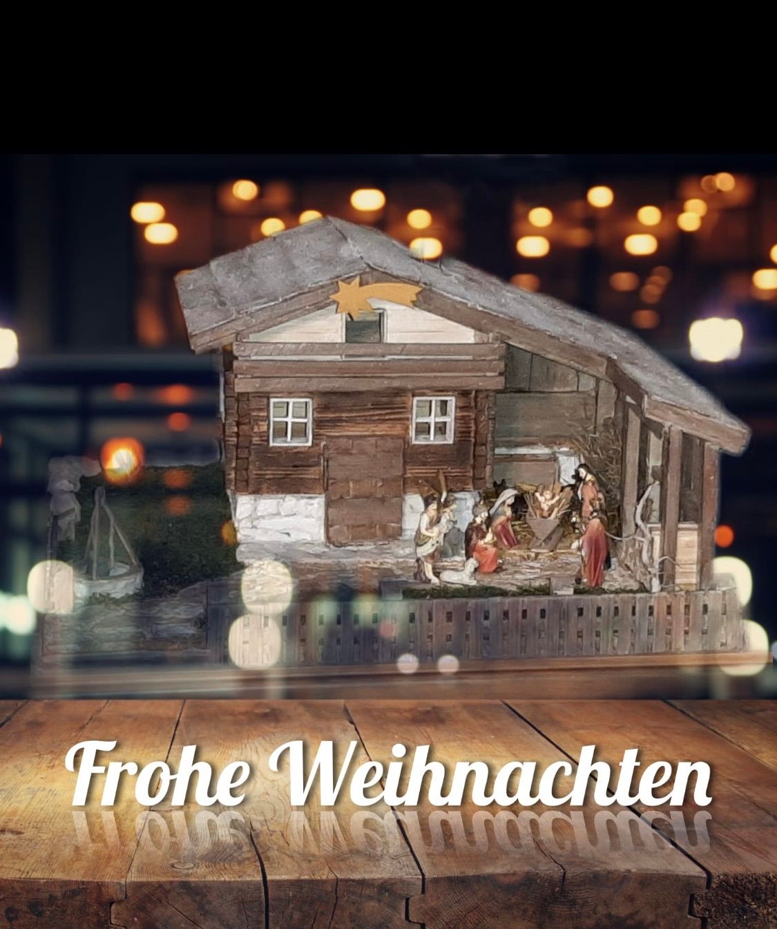 Ein kleines Haus mit einem Stern auf dem Dach, einer Krippe im Inneren und Weihnachtsdekoration. Darunter stehen die Worte 'Frohe Weihnachten'.