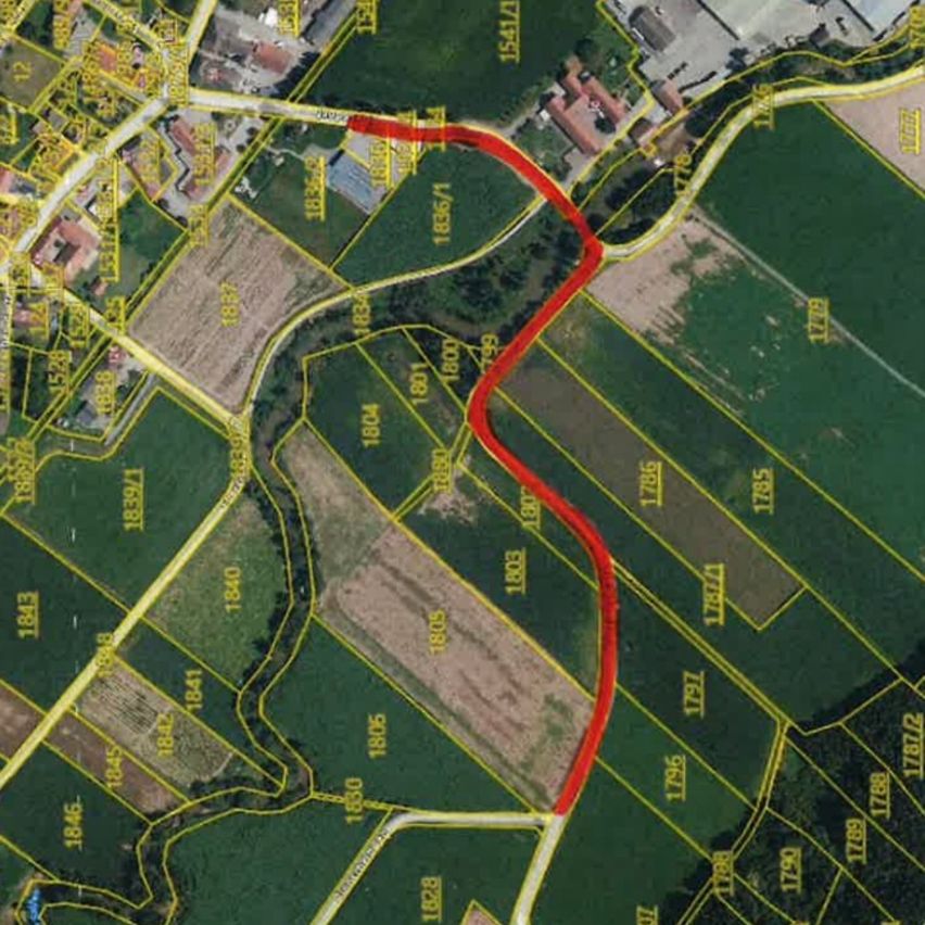 Eine Luftaufnahme einer Karte mit verschiedenen Grundstücken, die mit Zahlen beschriftet sind. Eine rote Linie zeigt eine Grenze oder einen Weg an. Grüne Felder sind durch gelbe Linien getrennt. Gebäude und Straßen sind sichtbar.