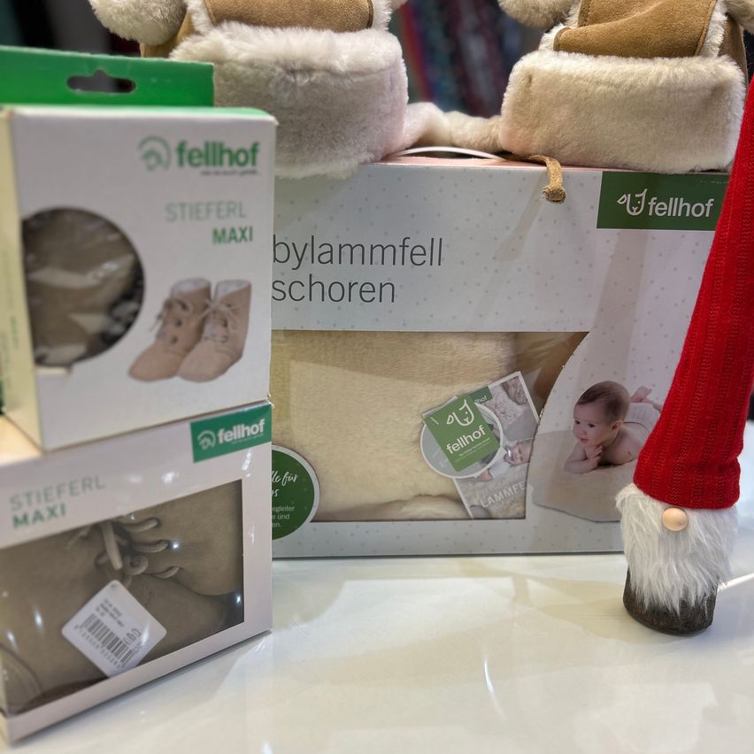 Drei Fellhof-Babyprodukte-Kisten im Schaufenster, darunter ein Paar Hausschuhe, Stiefel und eine Decke, mit einer kleinen Gnom-Figur im Vordergrund.