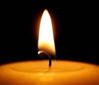 Eine brennende Kerze mit einer gelben Flamme leuchtet hell in der Dunkelheit. Der Kerzenwachs ist in einem kleinen Pool um den Docht geschmolzen.