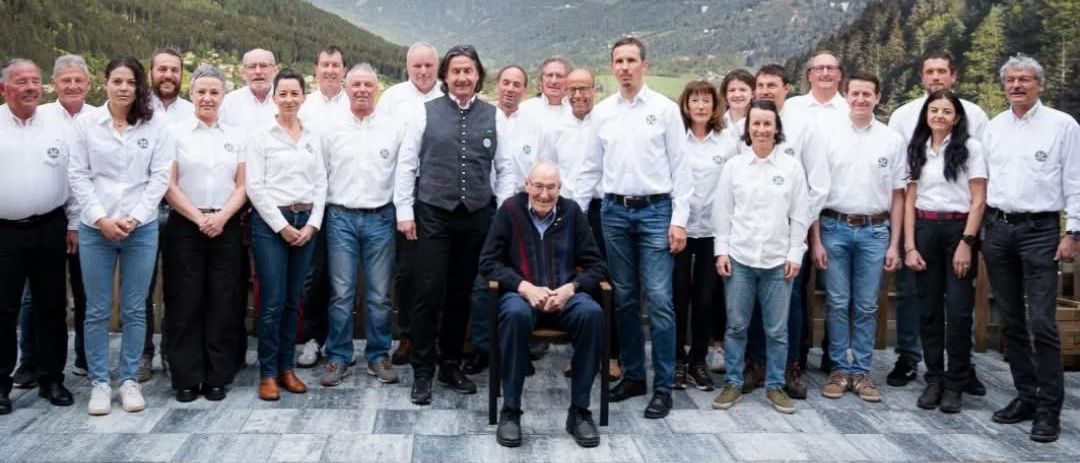 Eine Gruppe von Personen in weißen Hemden und Jeans posiert für ein Foto auf einer gefliesten Terrasse mit Bergen im Hintergrund.