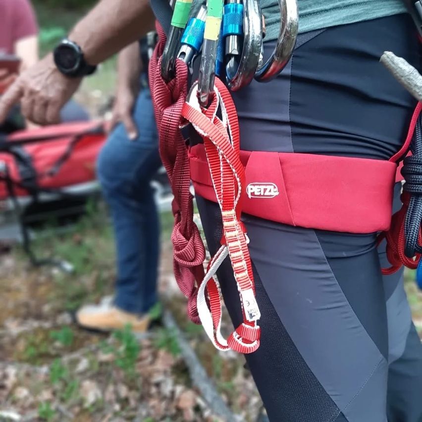 Ein Mann bereitet sich mit einem roten Gurt, PETZL-Logo und verschiedenen Kletterseilen und Karabinern um die Taille auf das Klettern vor.