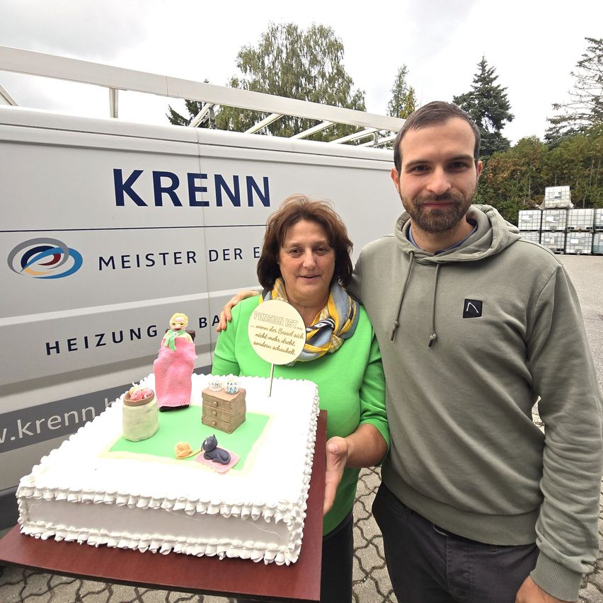 Ein Mann und eine Frau stehen neben einem Kuchen. Die Frau hält einen Kuchen mit einer Figur darauf. Sie lächeln beide. Dahinter steht ein Van mit der Aufschrift KRENN.