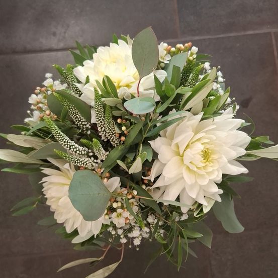 Ein Strauß weißer Blumen mit grünen Blättern, einschließlich Dahlien, ist auf einer gefliesten Oberfläche arrangiert.