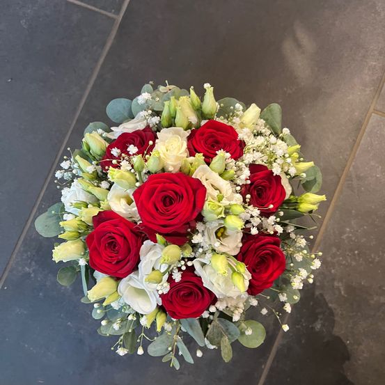 Ein runder Blumenstrauß mit roten, weißen und gelben Blumen, einschließlich Rosen und Babys Atem, auf einem gefliesten Boden.
