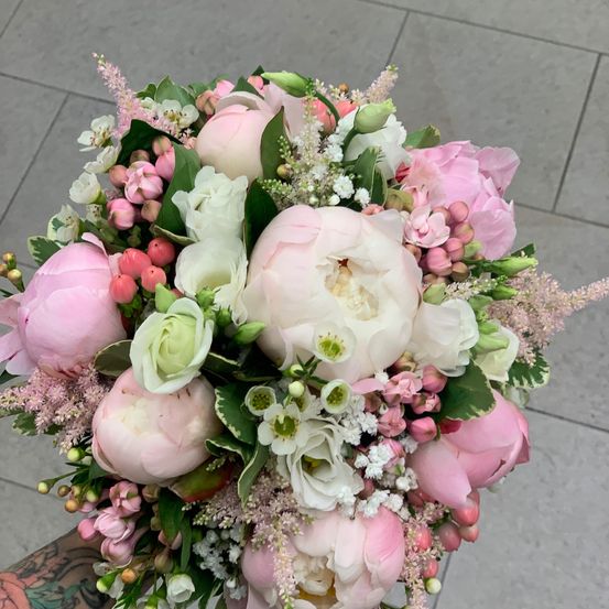 Ein Nahaufnahme eines farbenfrohen Blumenstraußes mit rosa und weißen Pfingstrosen, Rosen und Grünpflanzen auf einem gefliesten Boden.
