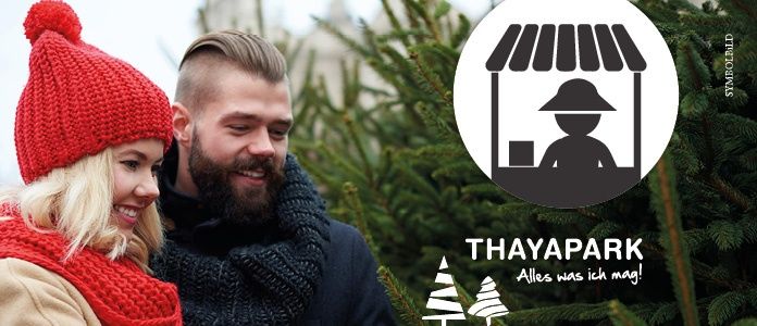 Ein Paar steht vor einem Weihnachtsbaummarkt und lächelt sich an. Der Mann trägt einen Bart und eine Schürze, während die Frau eine rote Mütze trägt. Der Markt hat einen Stand mit einer Silhouette einer Person.