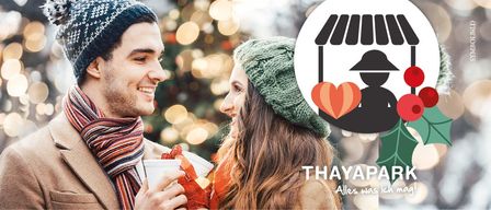 Ein Paar, das sich anlächelt und Kaffeetassen hält, mit einem Weihnachtsbaum im Hintergrund. Das Bild zeigt ein Logo für Thaypark.