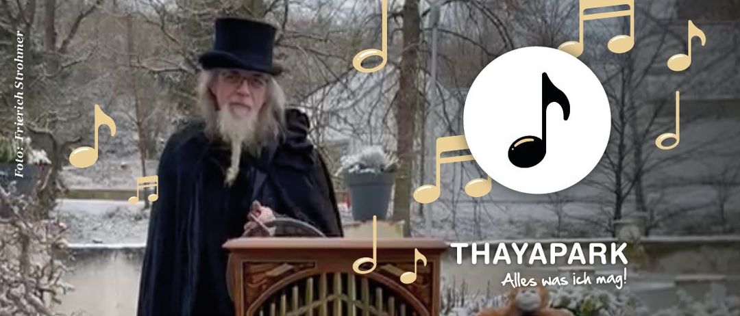 Ein alter Mann in einem Umhang und Hut steht vor einer Orgel, umgeben von Musiknoten, in einer verschneiten Landschaft. Der Text lautet 'THAYAPARK Alles was ich mag!'.