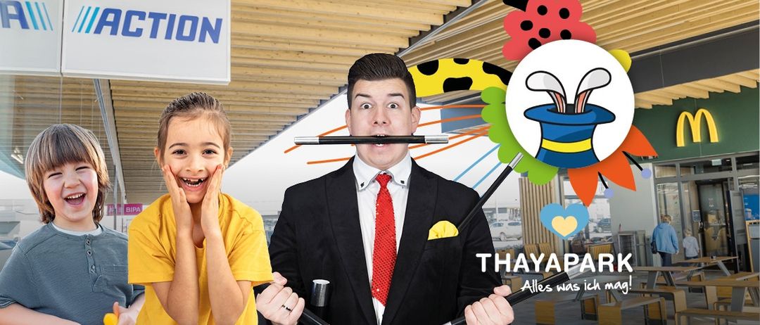 Ein Mann in Anzug mit einem Zauberstab im Mund und ein Mädchen lächelt mit den Händen auf dem Gesicht. Ein weißes Schild mit blauen Buchstaben, die 'ACTION' sagen, ist über ihnen.