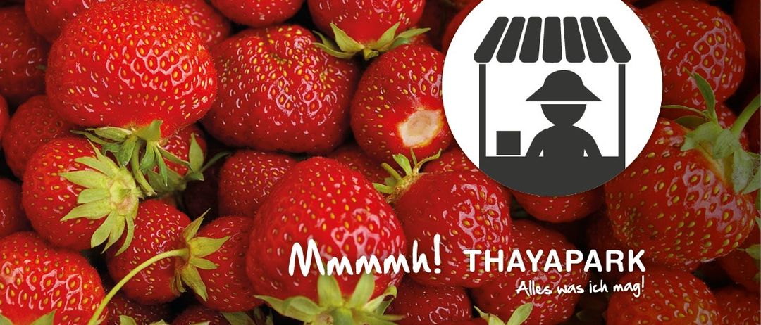 Eine Nahaufnahme von Erdbeeren mit einem Verkäuferstand-Symbol und Text 'Mmm! THAYAPARK Alles was ich mag!' auf Deutsch.