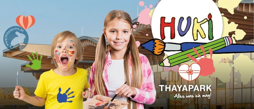 Zwei Kinder, ein Mädchen und ein Junge, stehen draußen. Das Mädchen malt auf einer Tafel und lächelt. Der Junge hat Farbe im Gesicht und schaut in die Kamera. Es gibt einen Text, der 'HUKi' und 'THAYAPARK' auf dem Bild steht.