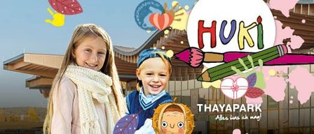 A poster featuring two children smiling in front of a building with the words 'THAYAPARK' and 'HUKi'. The children are surrounded by colorful illustrations of leaves, pencils, and a heart. The building has a modern architectural design.
