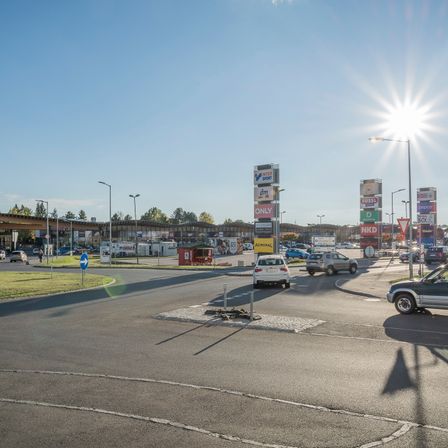 Eine Kreuzung mit einigen Autos und mehreren Werbetafeln, von denen eine Admiral sagt. Eine Person geht auf dem Bürgersteig auf der linken Seite. Die Sonne scheint hell.