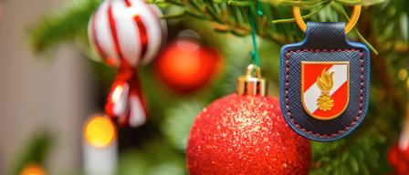 Ein Nahaufnahme eines Weihnachtsbaums mit einem roten Ornament, einem Abzeichen und anderen Ornamenten. Das Abzeichen zeigt ein Logo.