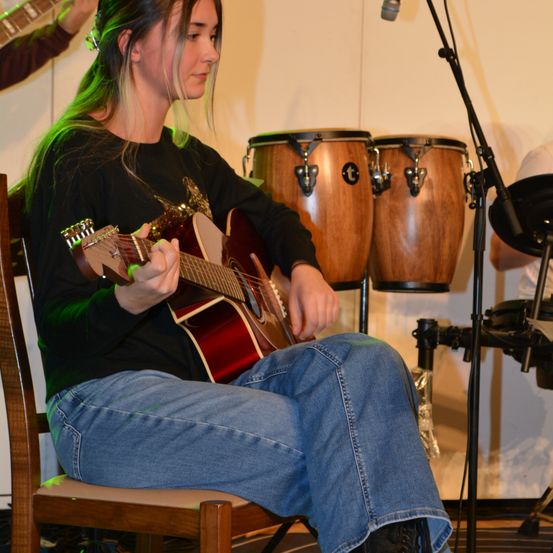 Bild enthält, Guitar, Musical Instrument, Person, Microphone, Chair, Jeans, Pants, Concert, Face, Shoe