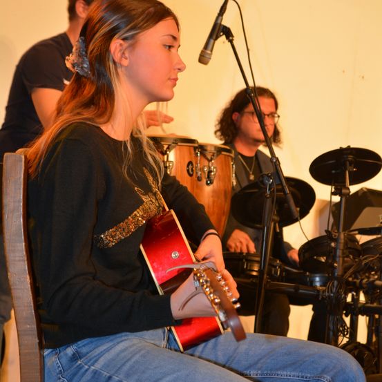 Bild enthält, Microphone, Adult, Female, Person, Woman, Guitar, Musical Instrument, Glasses, Necklace, Jeans