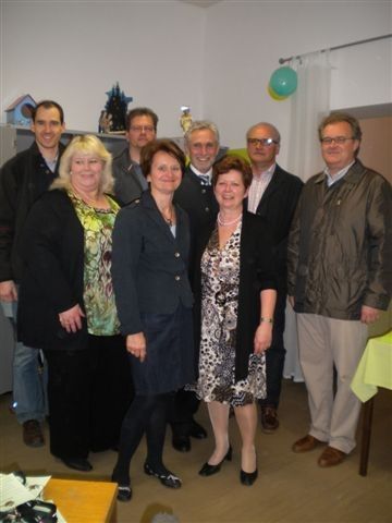 Eine Gruppe von Erwachsenen, sowohl Männer als auch Frauen, posieren für ein Foto im Innenbereich. Sie alle lächeln und stehen zusammen.