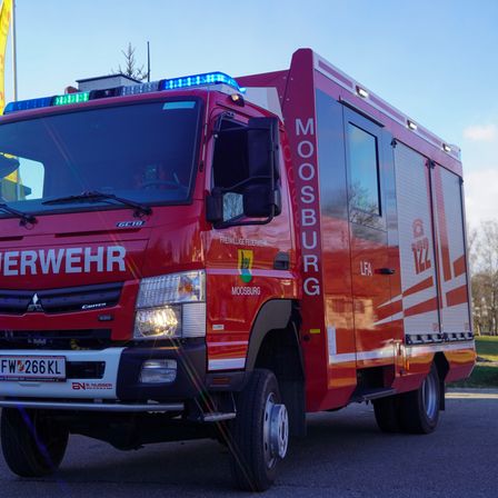 Ein roter Feuerwehrwagen mit der Aufschrift Moosburg steht im Freien. Der Wagen verfügt über Warnleuchten, ein Nummernschild mit der Nummer FW 266 KL und einen vorderen Kühlergrill mit der Aufschrift 'FREIWILLIGE FEUERWEHR'.