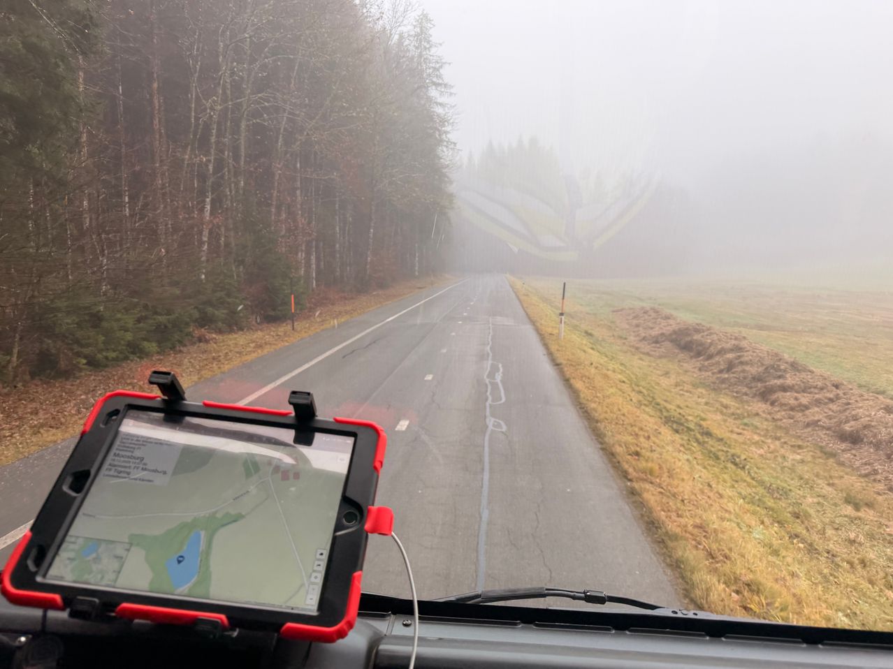 Eine neblige Straße mit einem Tablet, das eine Karte im Vordergrund anzeigt. Die Straße wird beidseitig von Bäumen gesäumt.