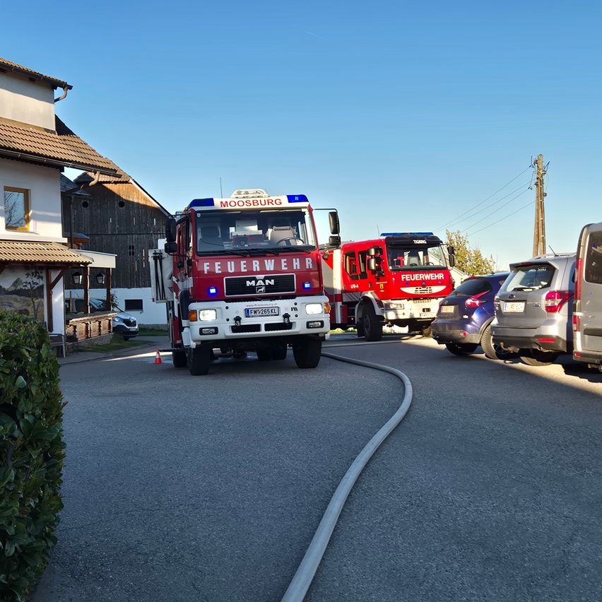 Ein roter Feuerwehrwagen aus Moosburg ist auf der Straße geparkt. Zwei weitere Feuerwehrwagen stehen dahinter, mit einem orangefarbenen Kegel in der Nähe.