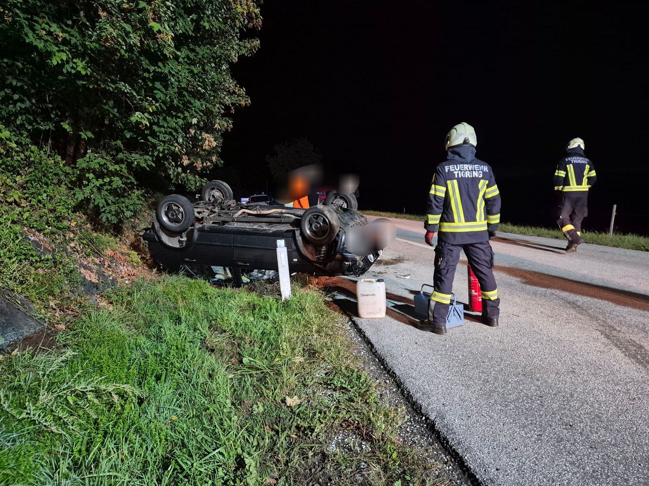 Ein Feuerwehrmann steht neben einem umgekippten Auto am Straßenrand bei Nacht.