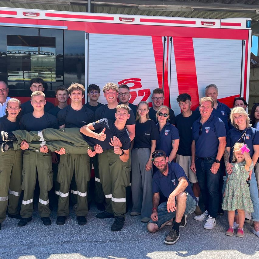 Eine Gruppe von Menschen in Uniformen posiert für ein Foto vor einem Feuerwehrwagen.