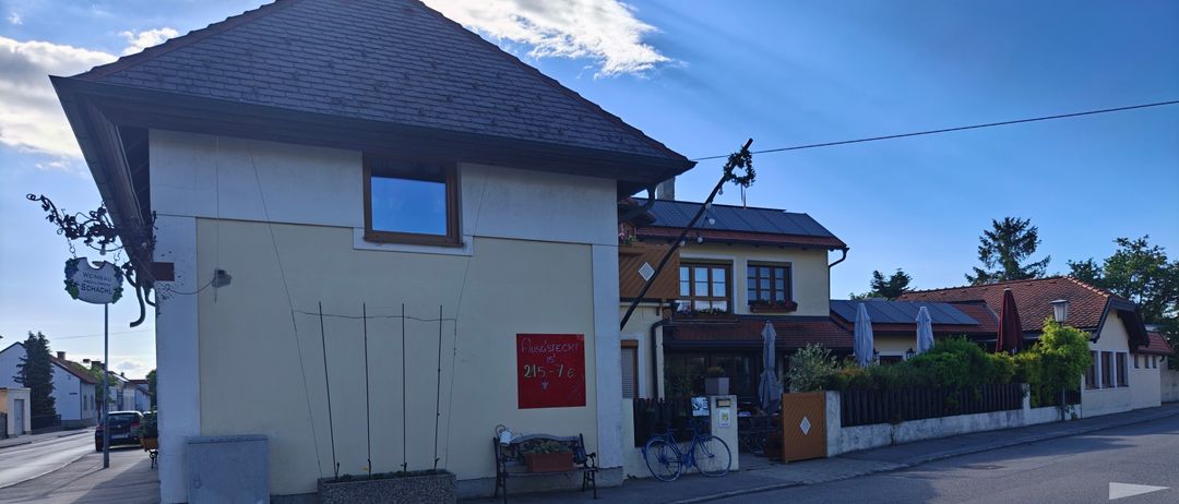 Ein Gebäude mit einem roten Schild, einer Bank und einem Fahrrad davor. Der Himmel ist klar mit einigen Wolken.