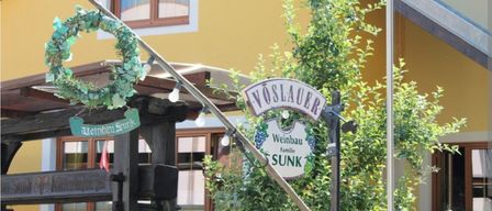 Ein Weinpresser und Schild für Voslauer Weinbau Familie sunk. Grüne Kränze schmücken die Presse. Eine rote Fahne ist in der Nähe.