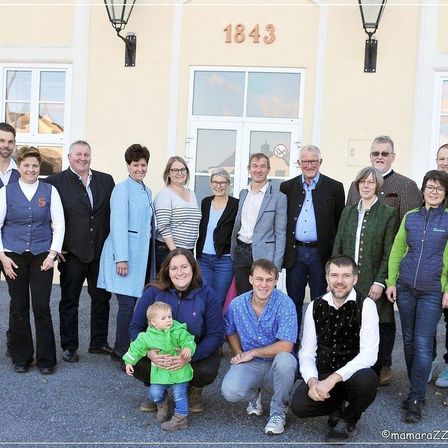 Eine Gruppe von Menschen in Geschäftskleidung steht vor einem Gebäude mit der Nummer 1843. Sie lächeln für ein Foto.