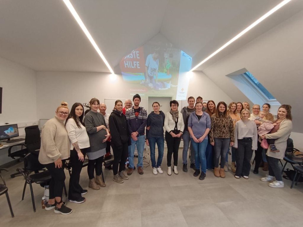 Eine Gruppe von Menschen steht drinnen vor einer Leinwand mit einem Mann. Sie alle lächeln für ein Foto.