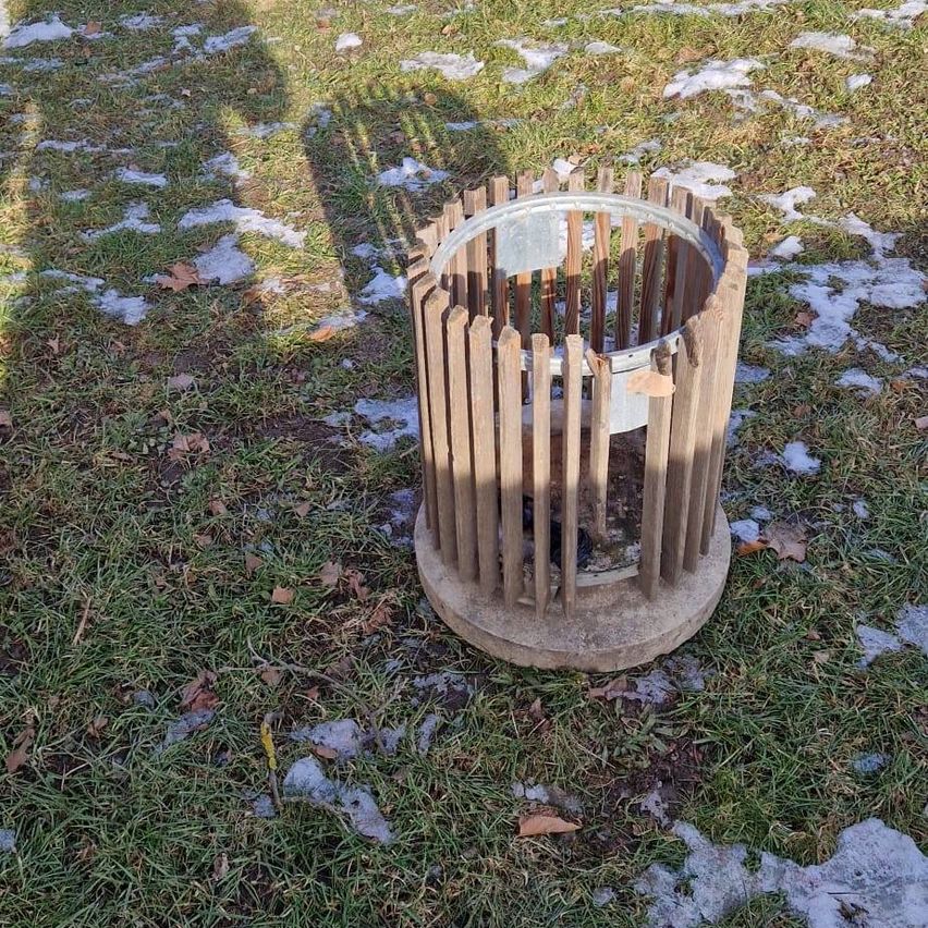 Eine Holzstruktur mit Metallrand liegt auf einem Rasenfeld mit verstreutem Schnee.
