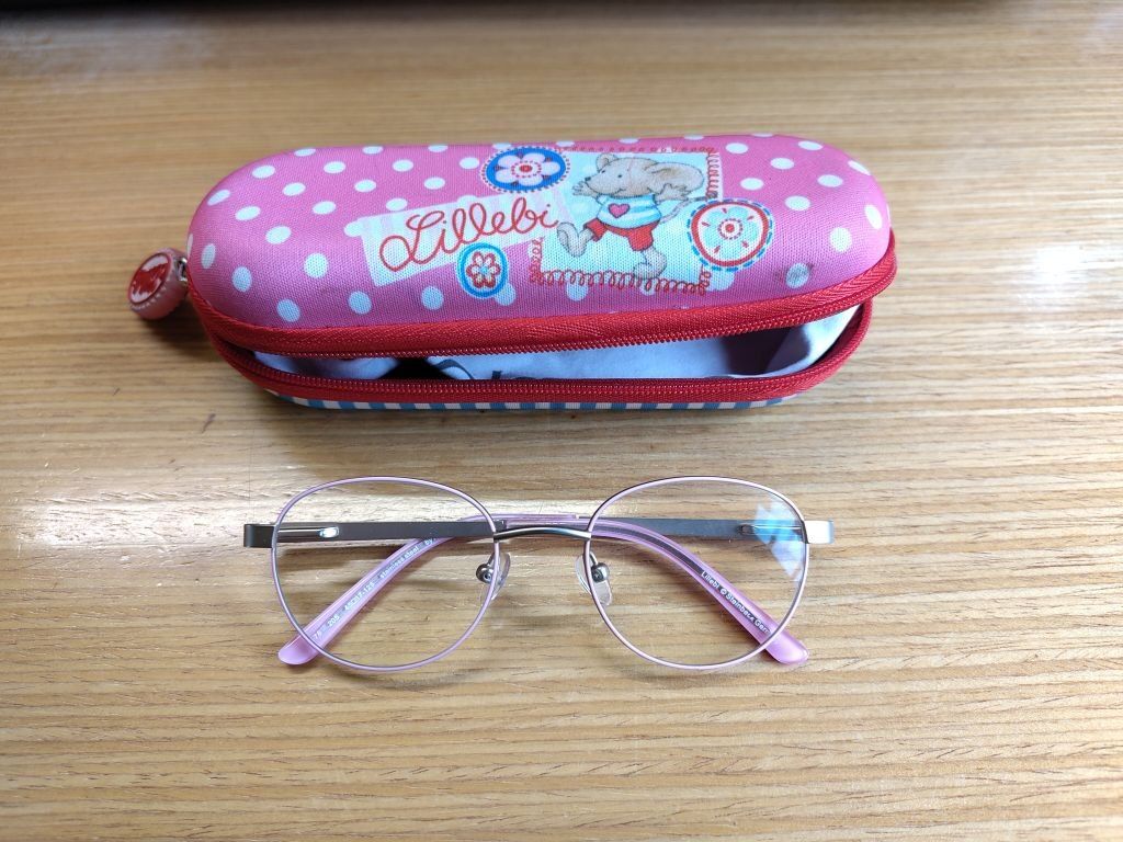 Eine Brille mit rosa Rahmen und einem rosa Etui mit Cartoon-Bären-Design. Das Etui befindet sich auf einer Holzoberfläche.