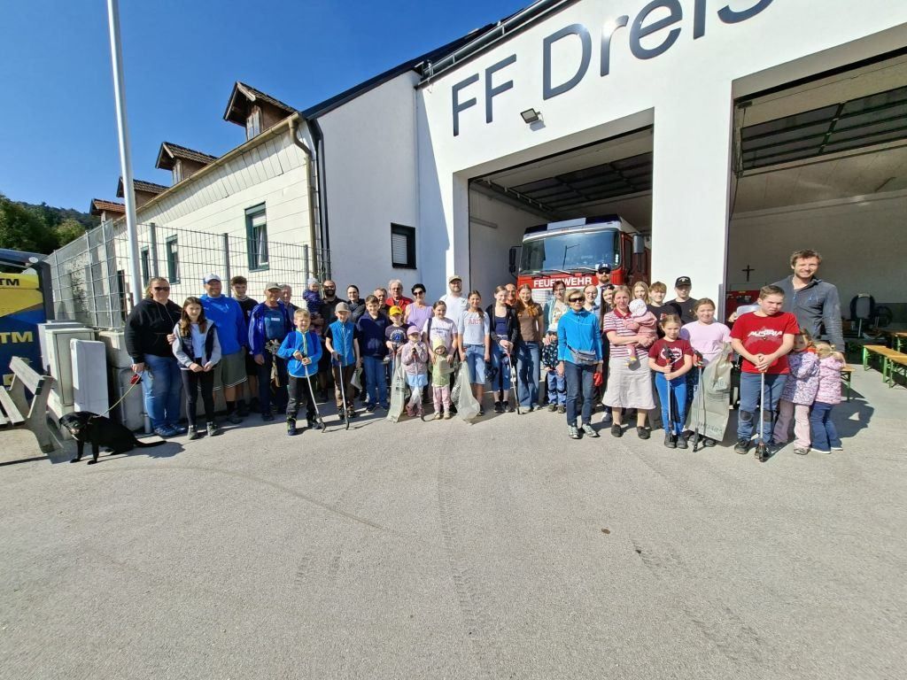 Eine Gruppe von Menschen steht vor einer Feuerwehrstation mit einem Feuerwehrauto. Sie lächeln und posieren für ein Foto.