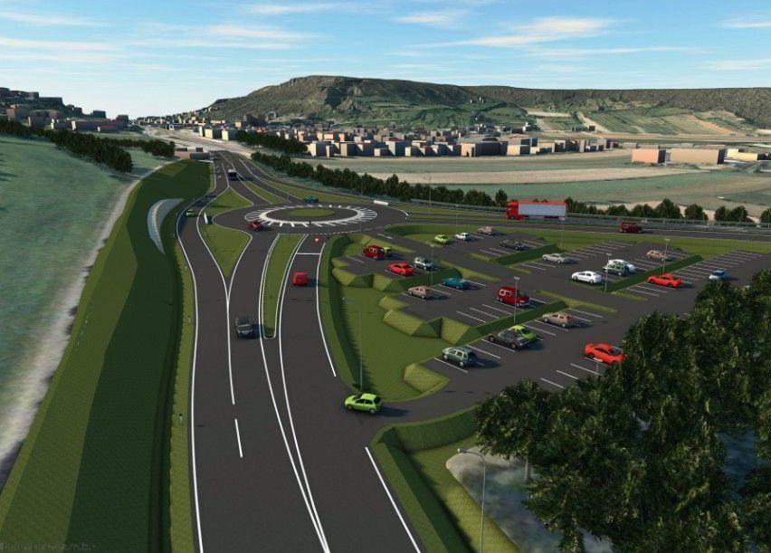 Eine Autobahn mit mehreren Spuren, auf der Autos, Lastwagen und ein Kreisverkehr zu sehen sind. Im Hintergrund befindet sich eine Stadt mit Gebäuden und einem Hügel.